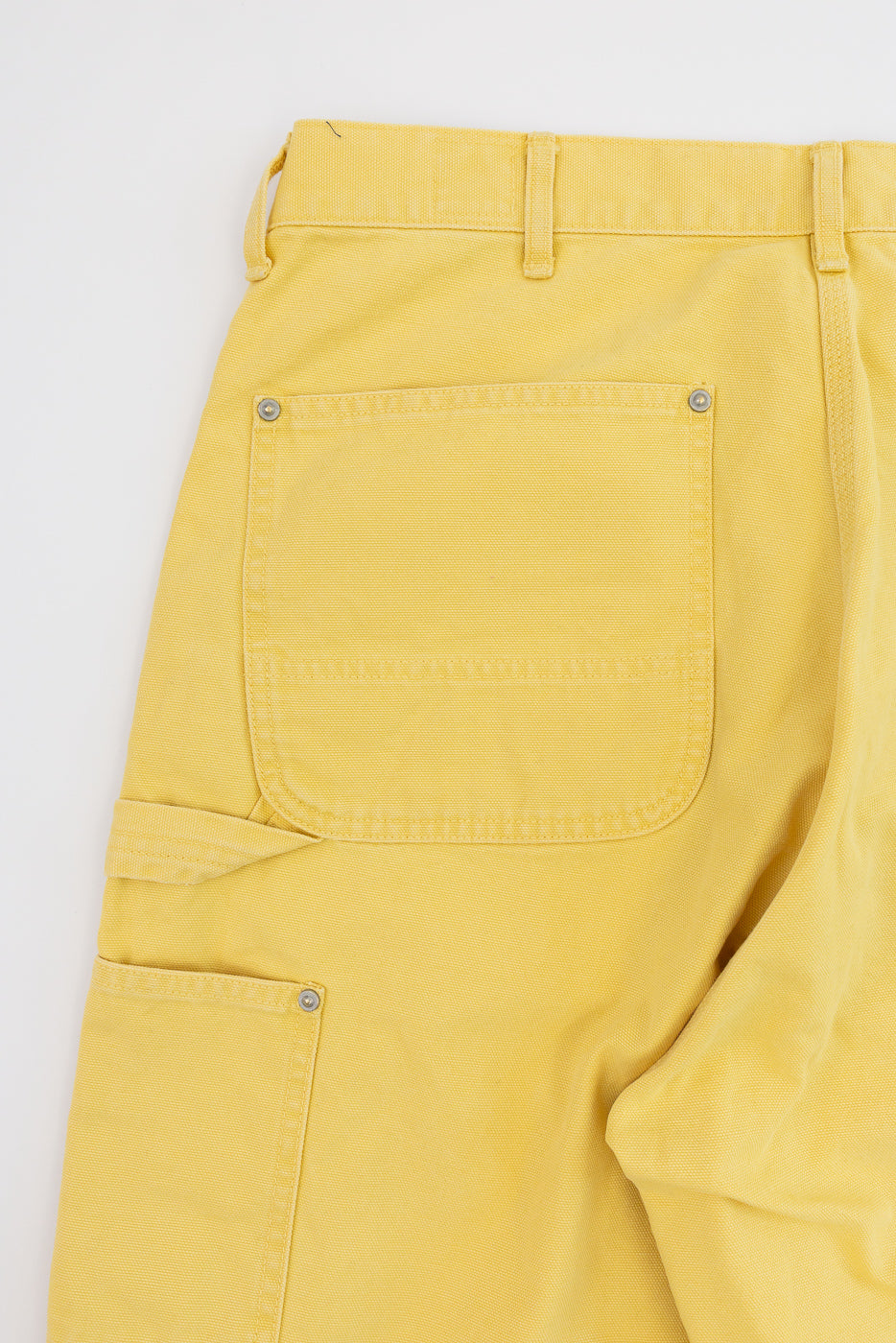 Close-up of yellow cargo pants back, showing rear pocket with metal rivets and fabric texture