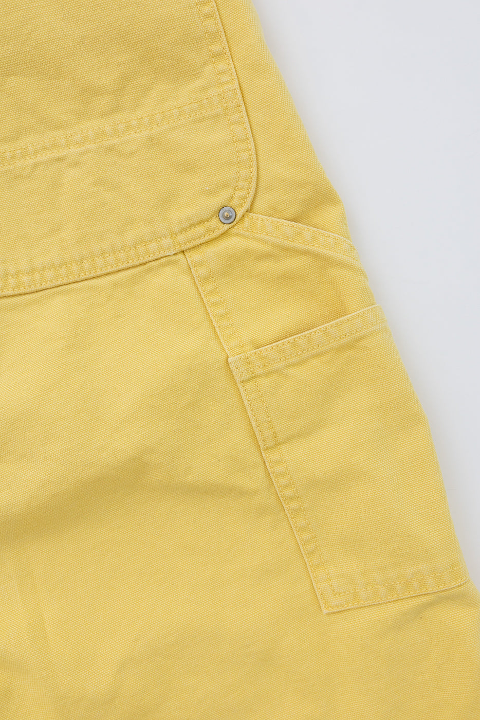 Close-up front view of yellow cargo shorts showing flap pocket with metal snap, fabric texture, and stitching details