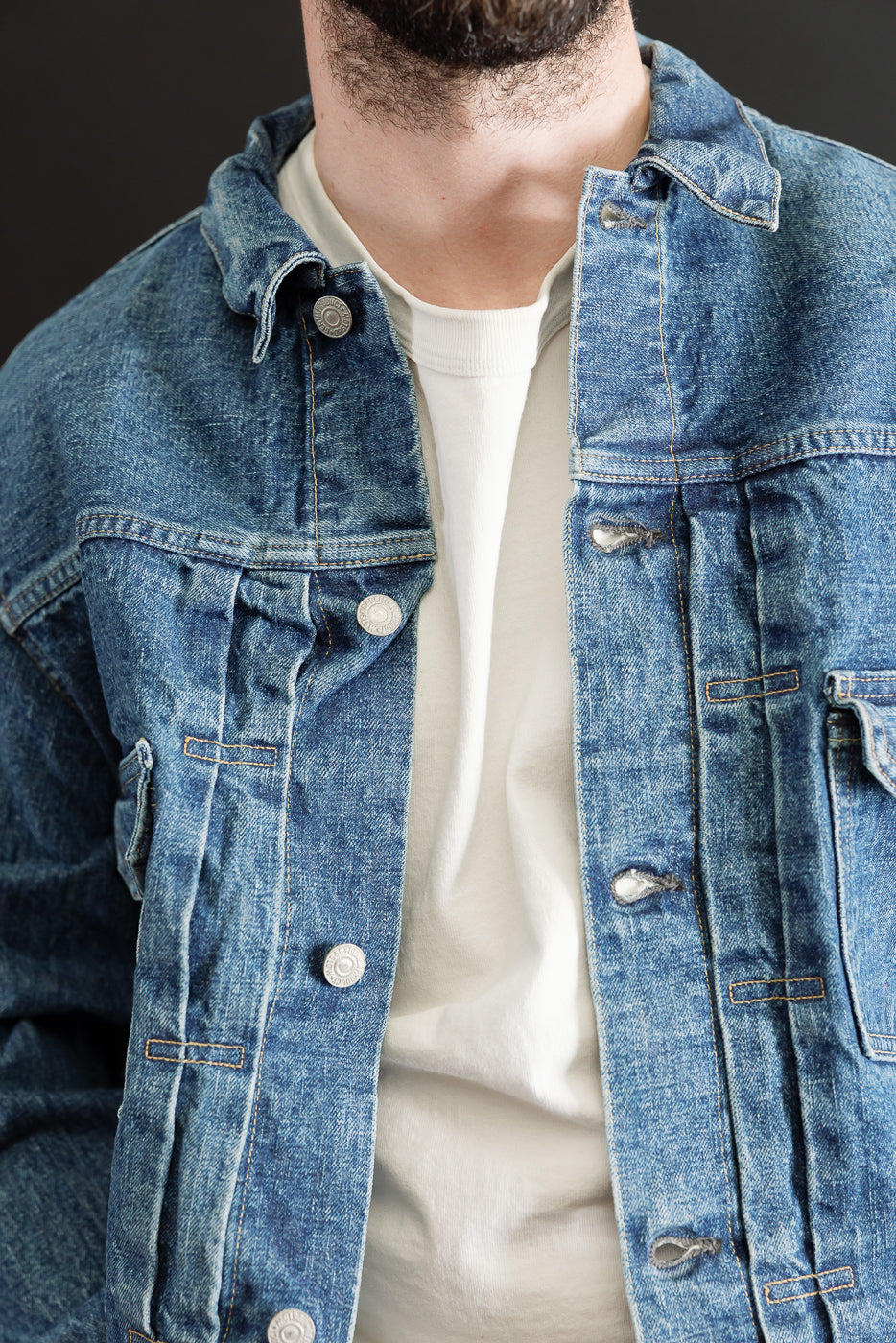 Close-up front view of a blue denim jacket on a male model, showing button details and collar.