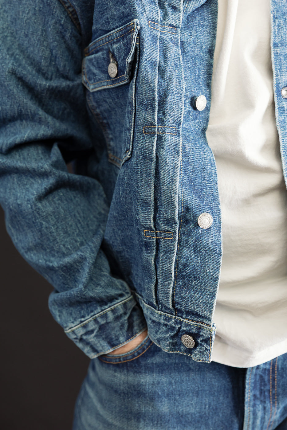 Close-up, front view of a blue denim jacket showing metal button details and fabric texture.