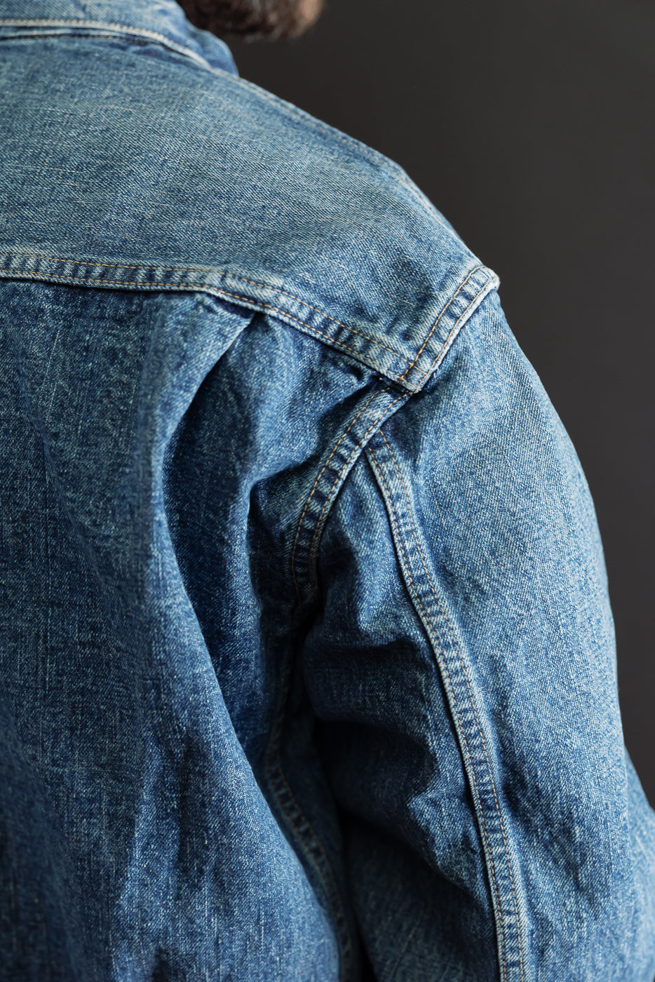Close-up view of the back and right shoulder of a blue denim jacket, showing seam detail.