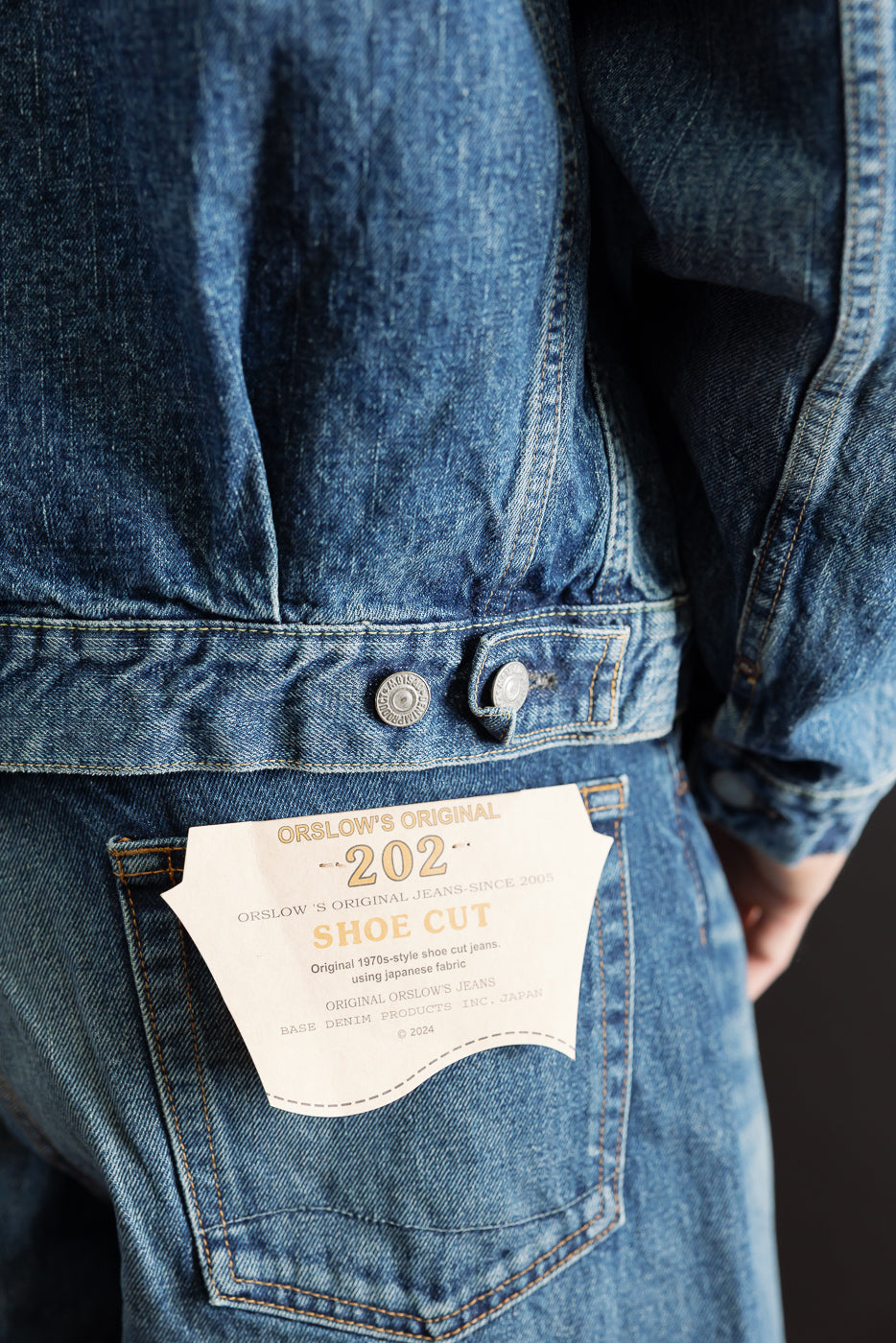 Close-up back view of blue denim fabric showing the rear pocket and a white Orslow brand tag.