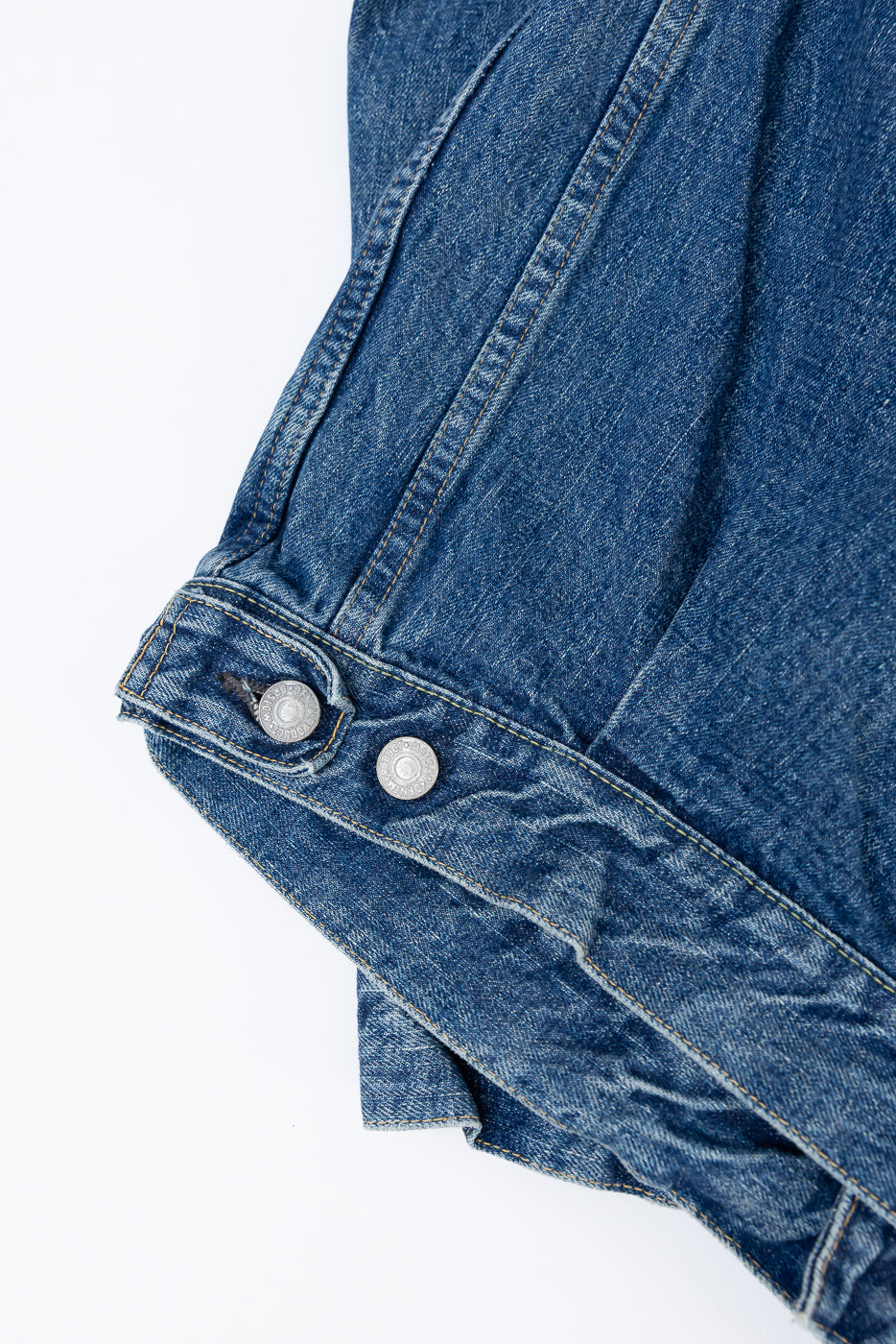 Close-up of the front waistband and silver buttons on a blue denim jacket.