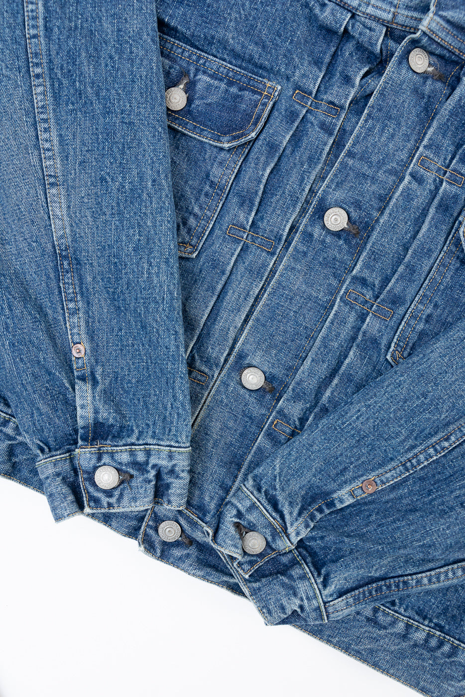 Close-up flat lay of the front of a blue denim jacket showing chest pocket and silver buttons.
