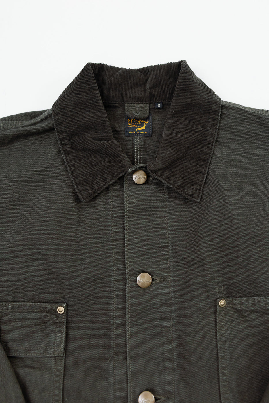 Close-up of the front top of a dark olive jacket featuring a corduroy collar, button, and tag.
