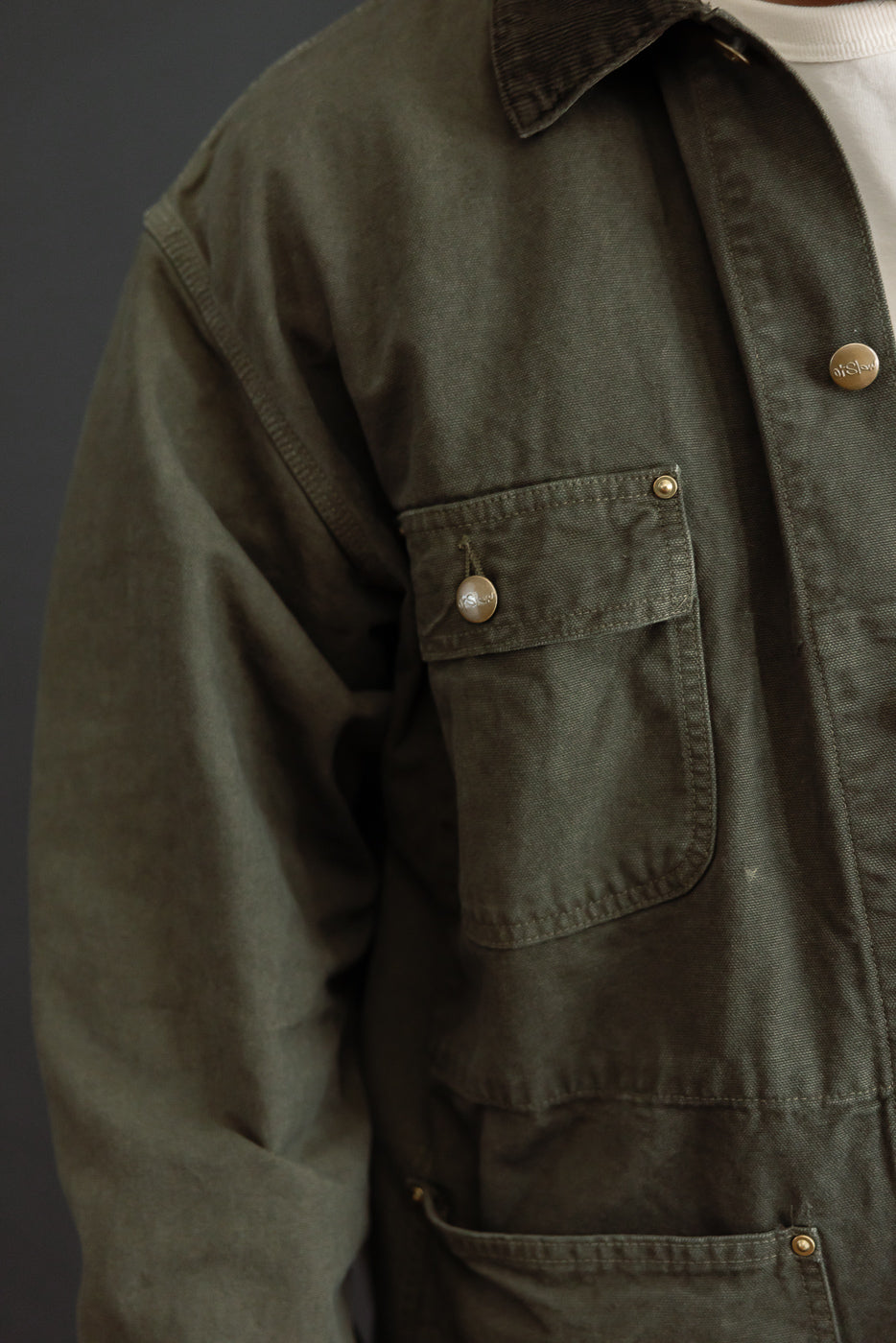 Close-up of left chest pocket on an olive green jacket worn by a male model, 5'9