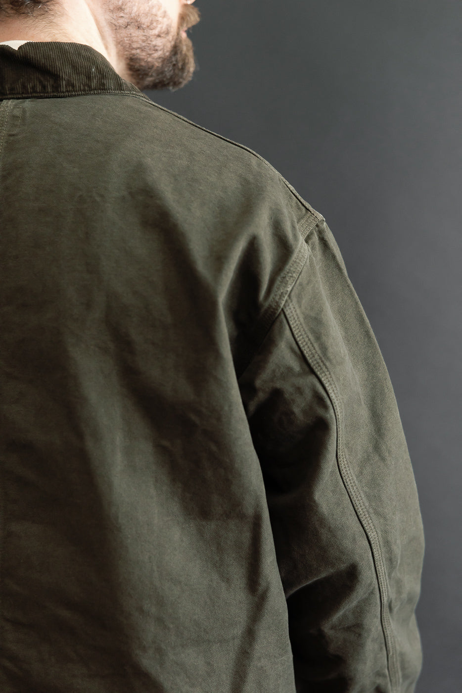 Close-up back view of a male model wearing an olive green cotton jacket showing the shoulder and collar.