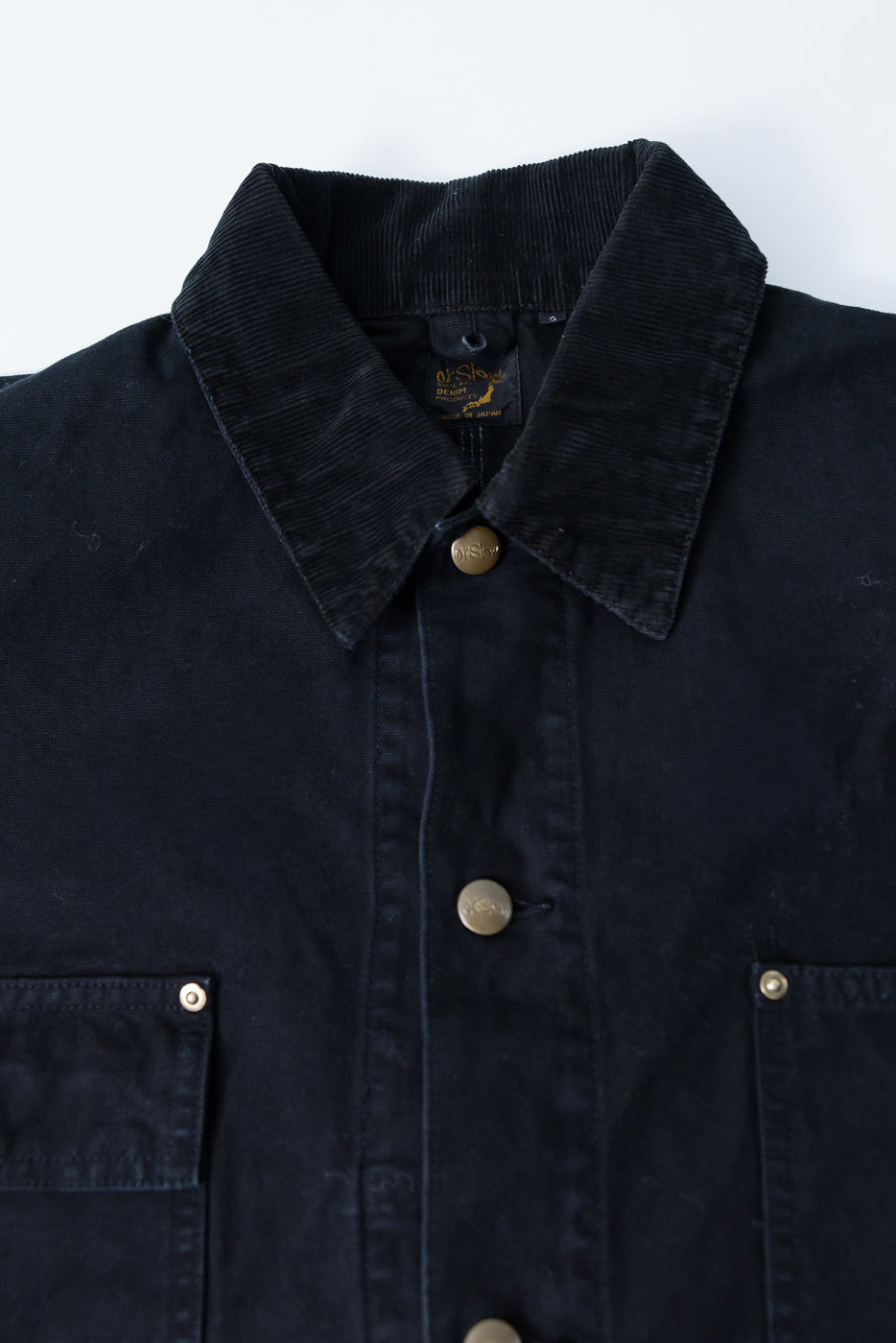 Close-up front of orSlow black coverall jacket, corduroy collar, brass buttons, chest pockets