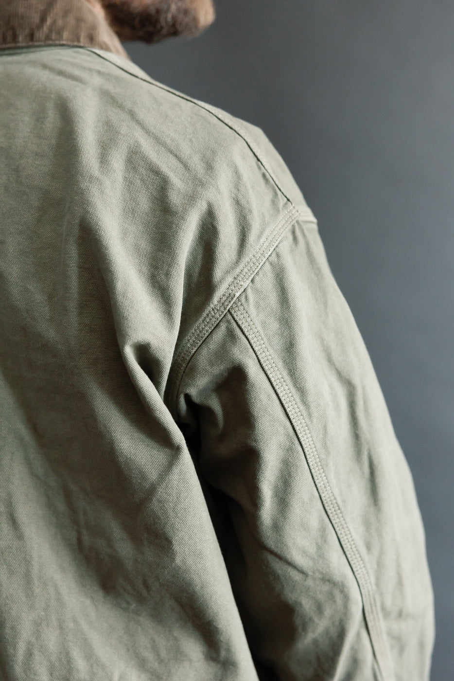 Close-up of male model's back shoulder wearing army green orSlow relaxed fit coverall jacket, highlighting fabric texture and seam details.
