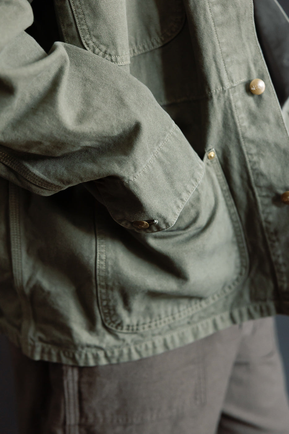 Close-up of orSlow Relaxed Fit Coverall Jacket in army green, showing front pocket, button details, and sturdy fabric texture, modeled by athletic male, 5'9