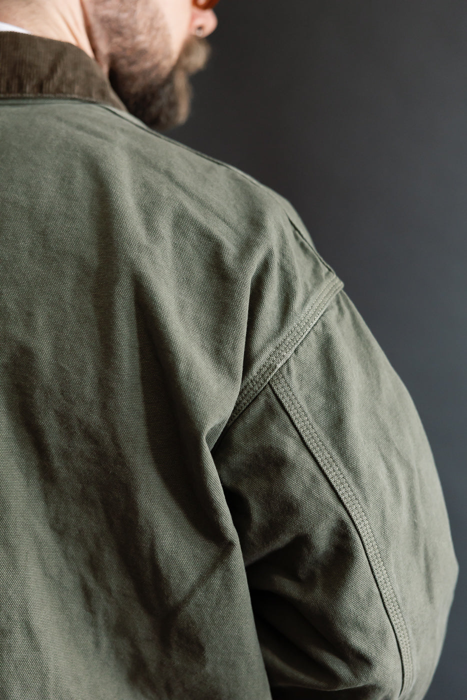 Close-up of army green coverall jacket shoulder and back seam on male model, athletic build