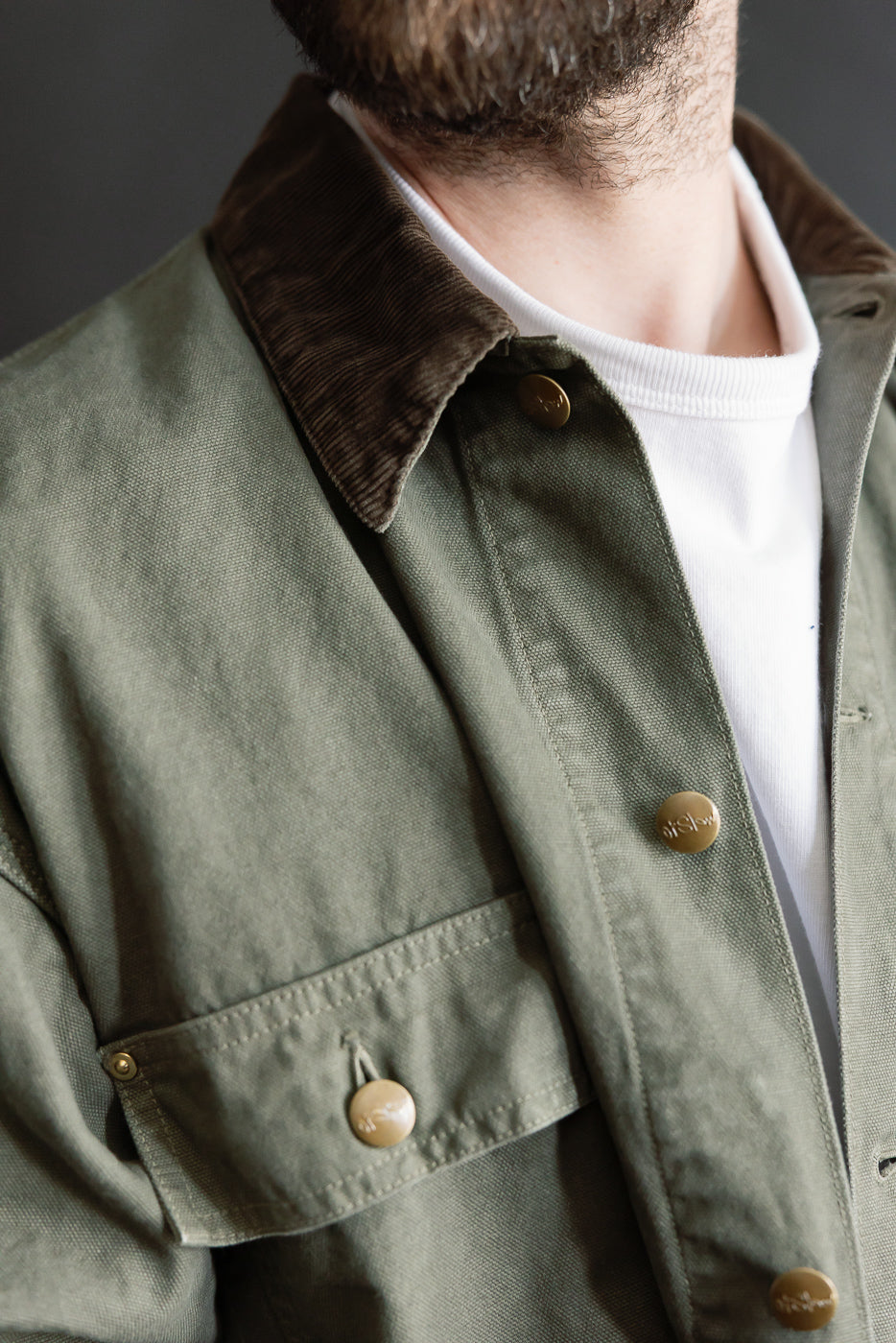 Close-up of front left chest area on orSlow army green coverall jacket, corduroy collar, snap buttons, worn by male model 5'9