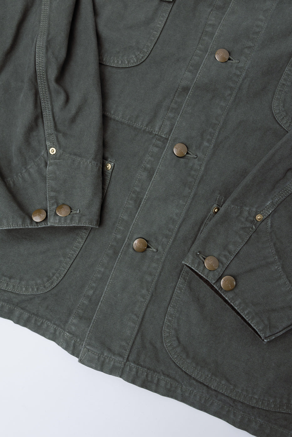 Close-up of front lower section, sleeve, and pockets on orSlow army green coverall jacket showing metal buttons and canvas texture.