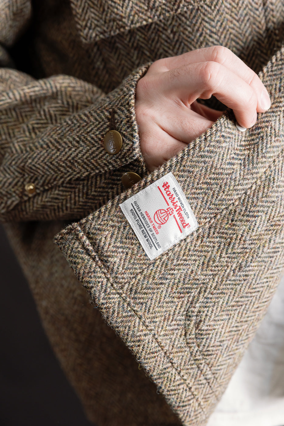 Close-up of Harris Tweed tag and metal buttons on orSlow khaki coverall jacket sleeve, herringbone wool fabric.