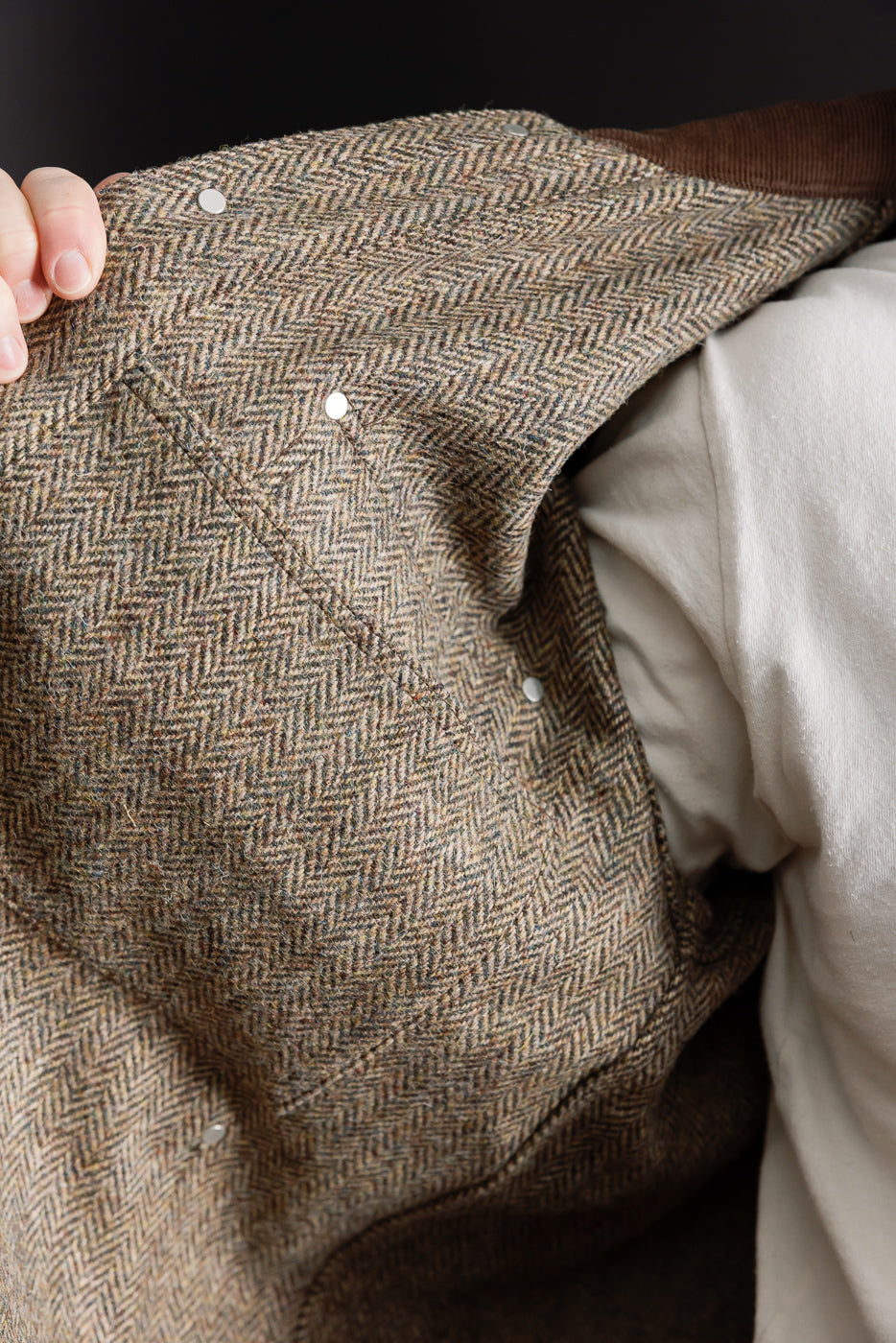 Close-up of inside front chest of Harris Tweed khaki coverall jacket showing herringbone texture and metal snap buttons at Dant.