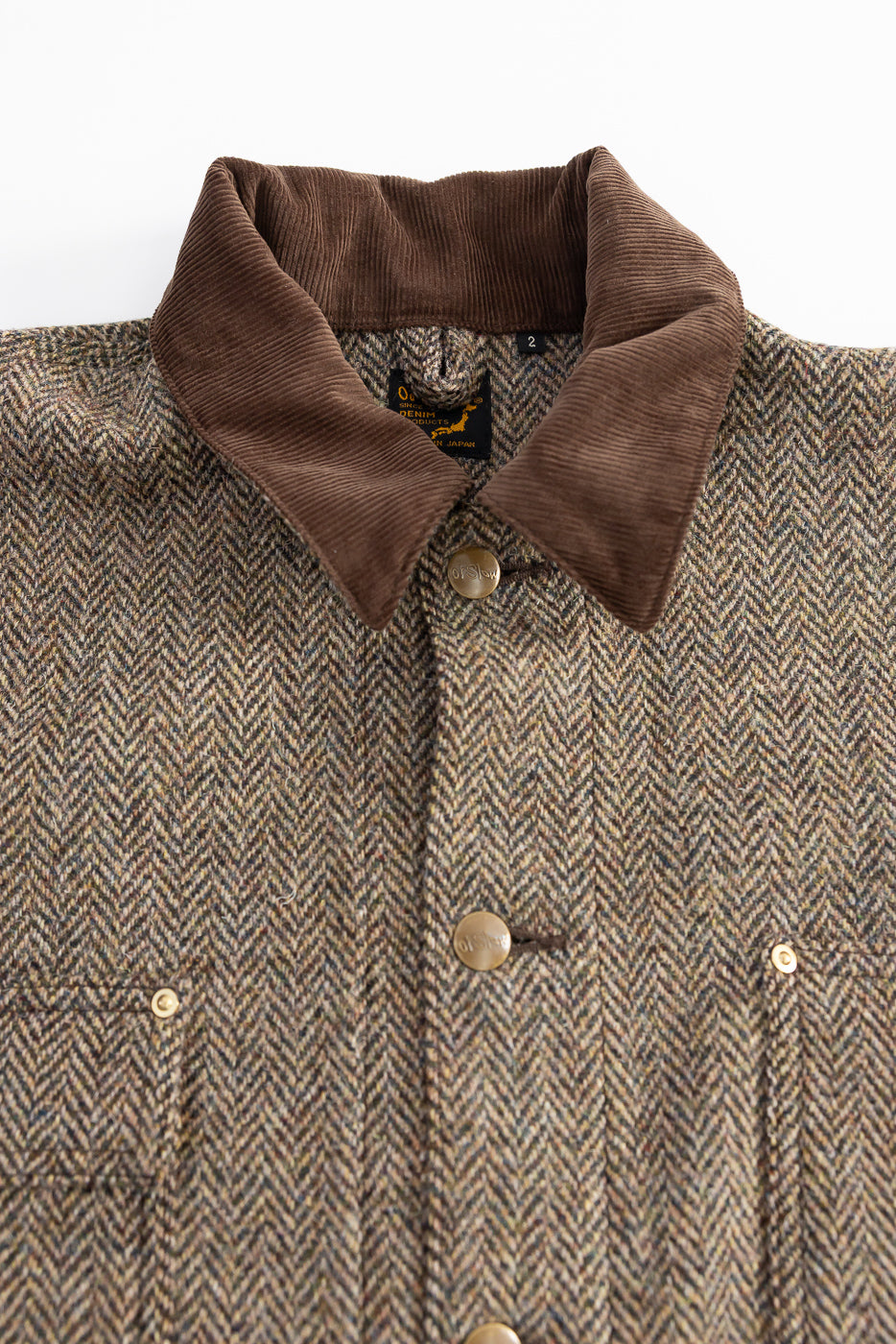 Close-up of orSlow Harris Tweed coverall jacket front, showing brown corduroy collar, herringbone wool fabric, brass buttons, and chest pockets. Contemporary casual outerwear at Dant Indianapolis.