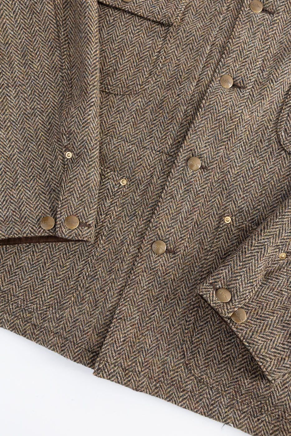 Close-up detail of front of khaki herringbone tweed coverall jacket with metal snap buttons