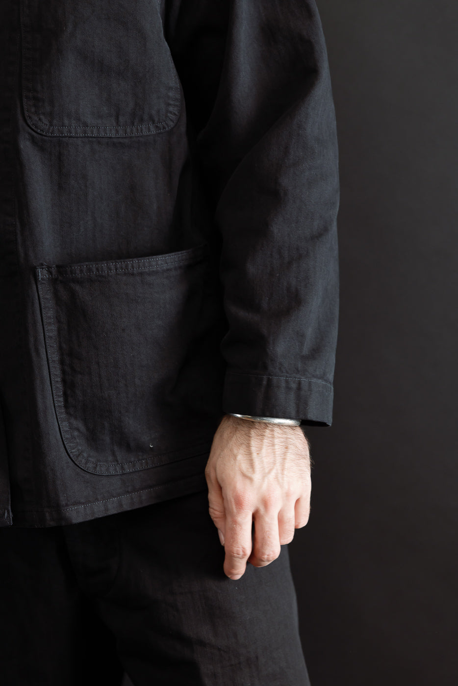 Close-up front view of a male model's hand and the side pocket of a black cotton chore coat.