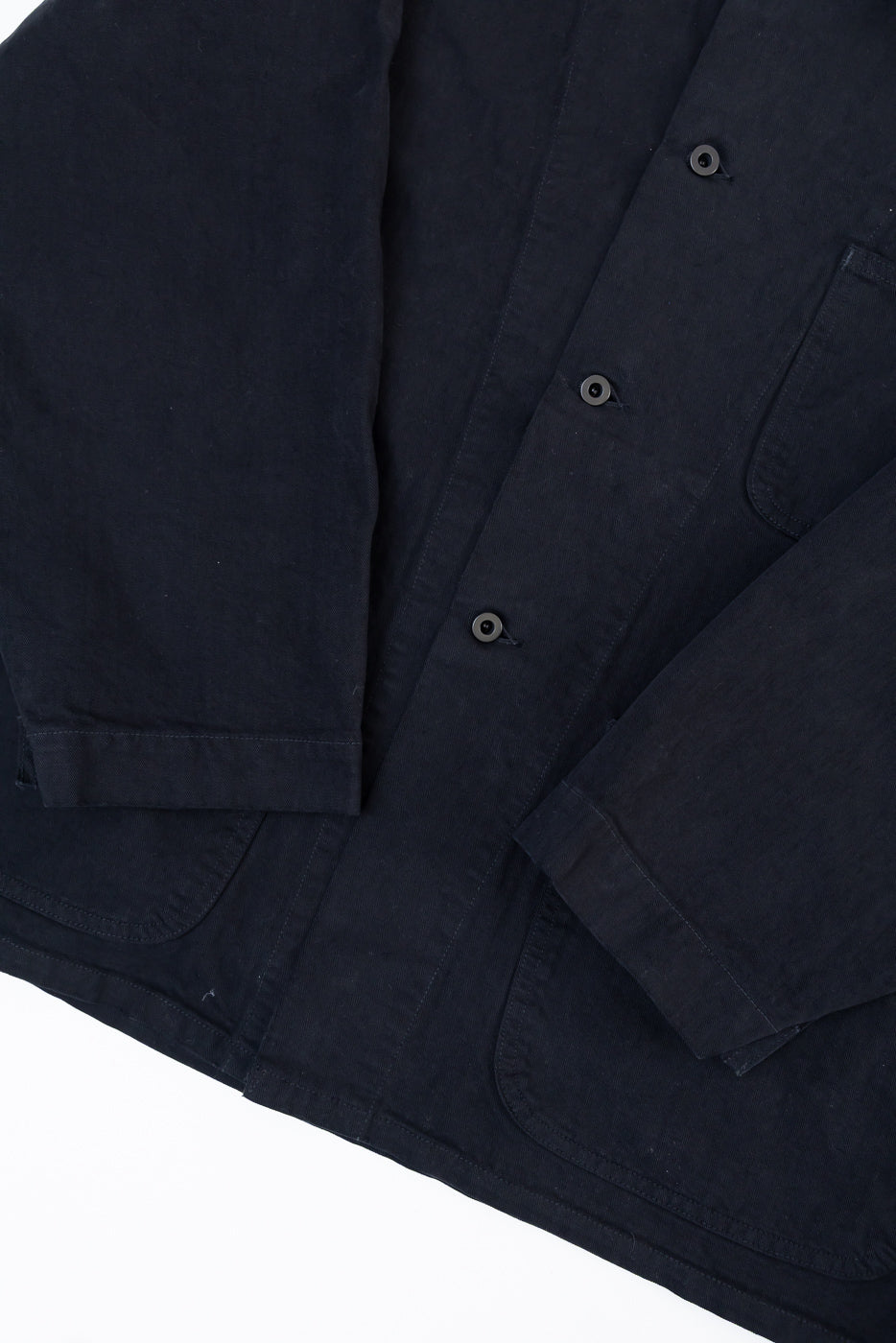Flat lay, front view close-up of navy blue canvas jacket showing button placket and pocket detail.