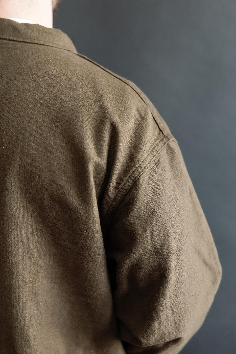 Close-up of orSlow coffee brown moleskin work jacket shoulder and sleeve, rear view, on athletic male model