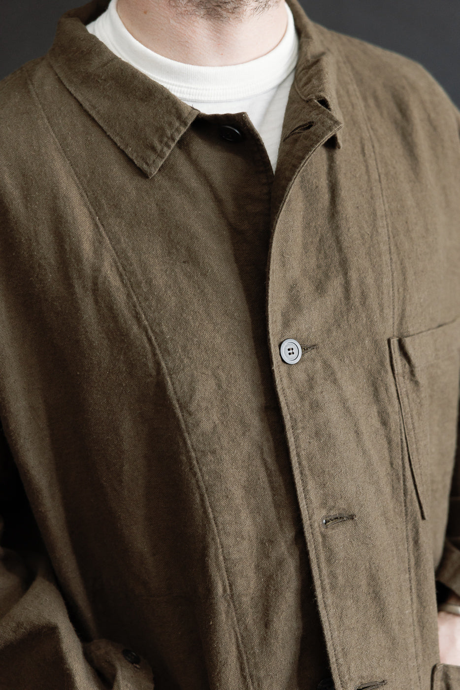 Close-up front of coffee brown moleskin work jacket on male model, showing collar, chest pocket, and button details; model is 5'9