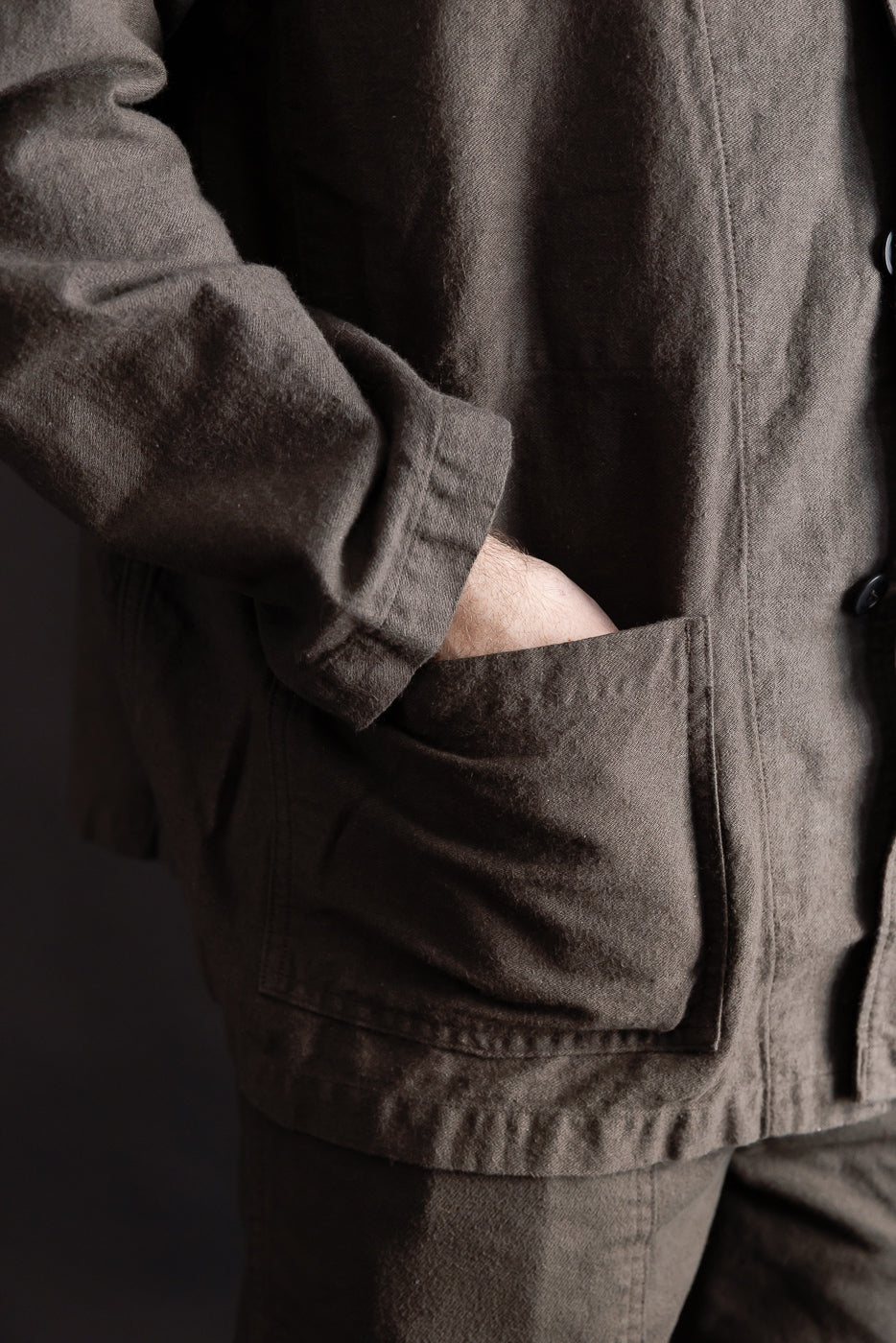 Close-up of male model wearing orSlow charcoal moleskin work jacket, front pocket detail shown, 5'9