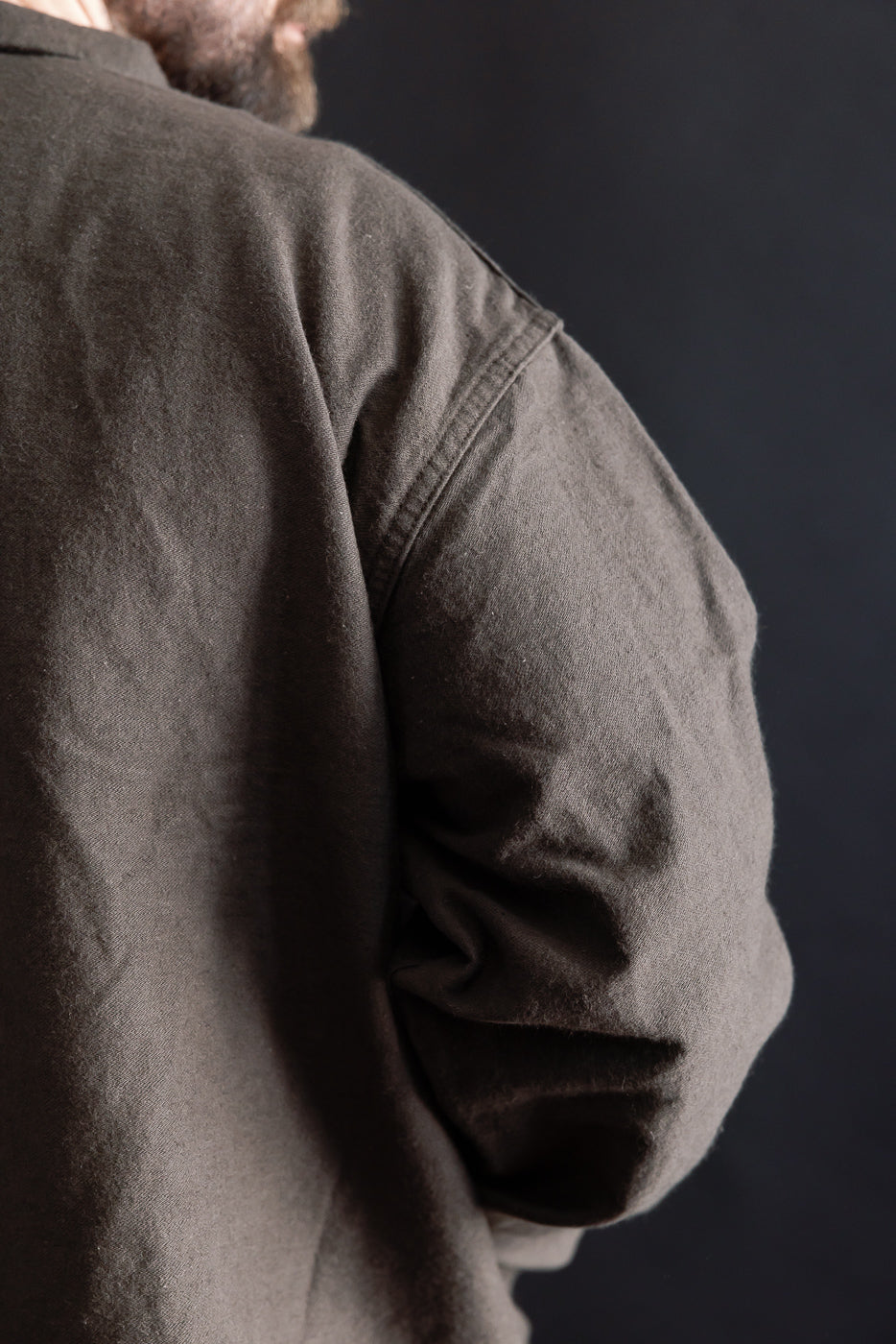 Close-up of male model's shoulder in Orslow charcoal moleskin work jacket, back side, showing fabric texture. Model is 5'9
