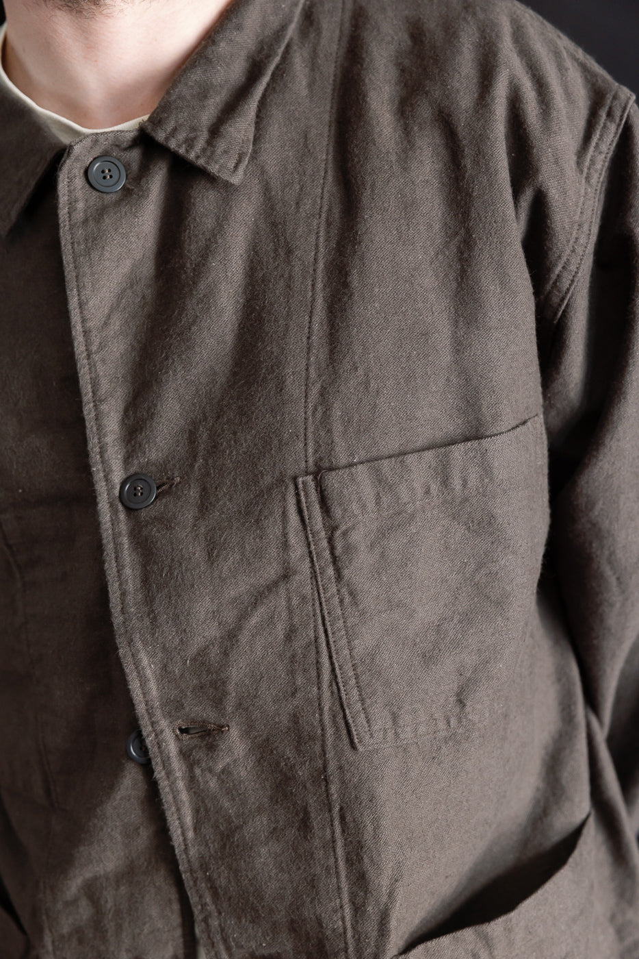 Close-up front of charcoal moleskin work jacket, showing button, collar, pocket; male model 5'9