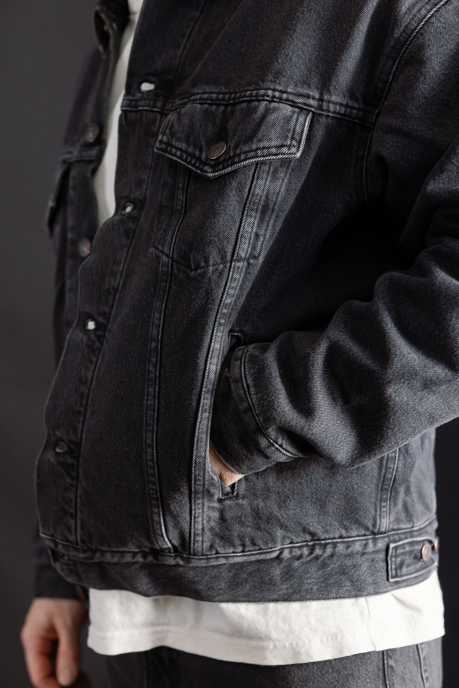 Close-up front view of black denim jacket chest and pockets on male model, 5'9