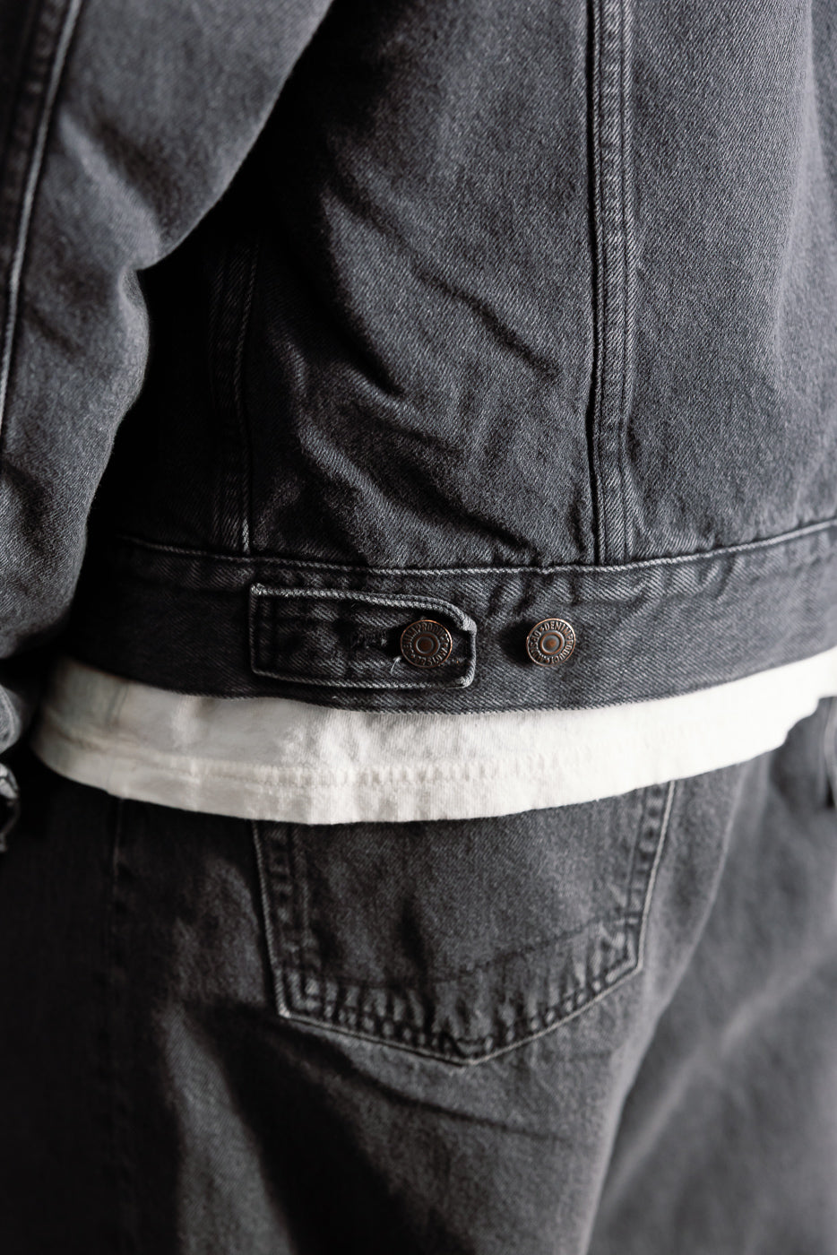 Close-up of back waist detail and buttons on black denim jacket, male model, Dant apparel