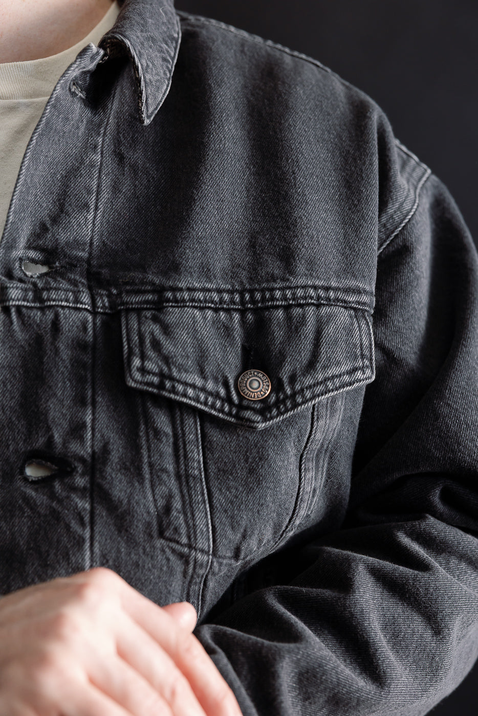 Close-up of front chest pocket, collar, and button details on black denim jacket, worn by male model, athletic build.
