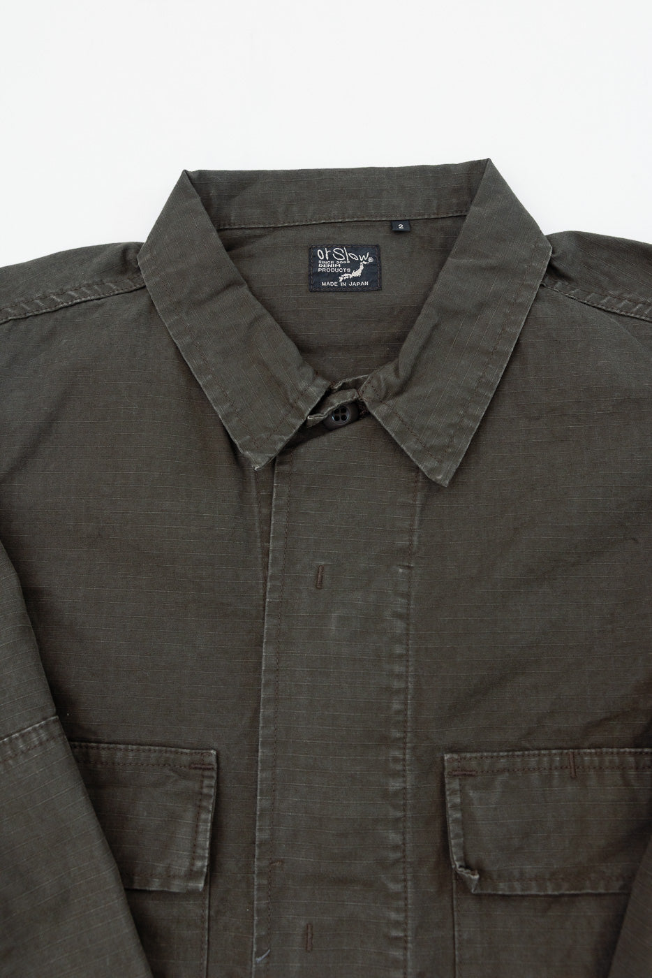 Close-up front view of olive green jacket showing collar, button, and fabric texture.