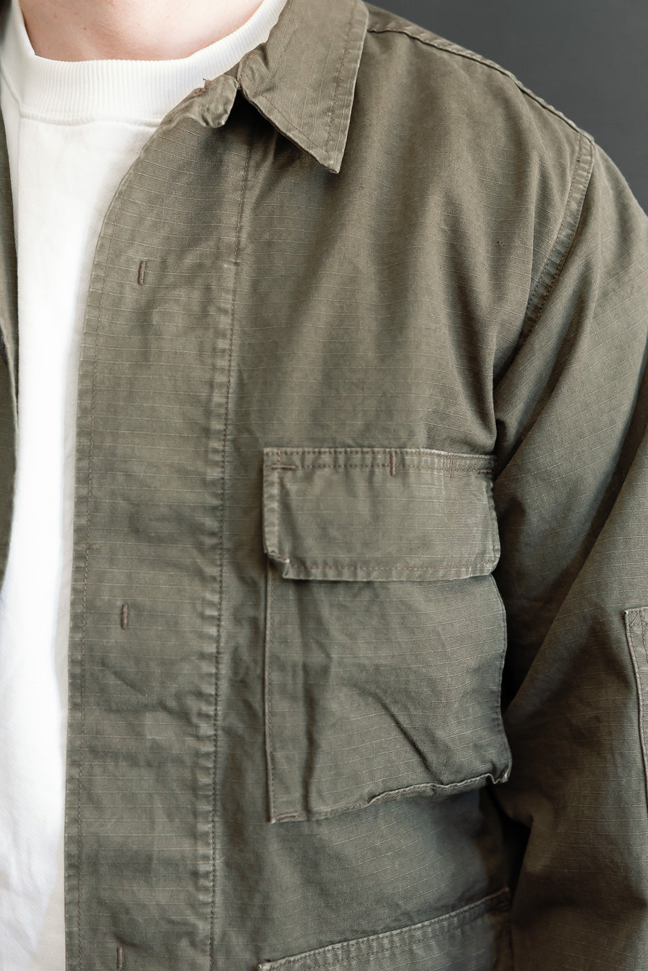 Close-up of the front left chest and pocket of an olive green cotton utility shirt on a male model.