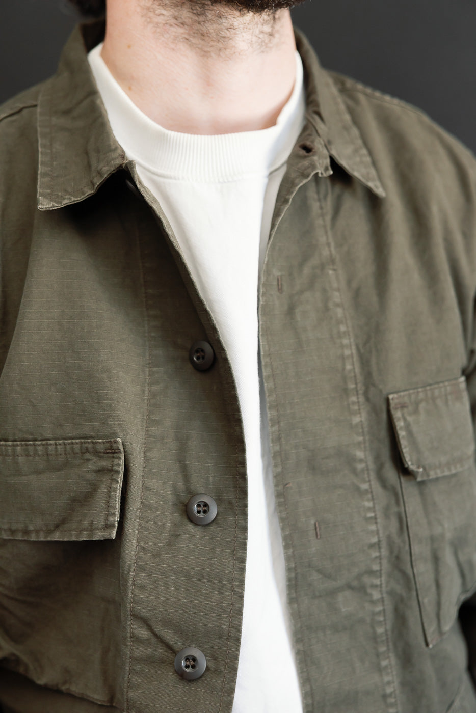 Close-up front view of a male model wearing an olive green cotton shirt over a white t-shirt.