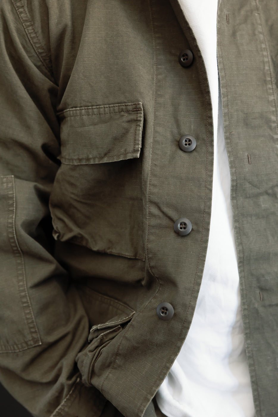 Close-up front view of an olive green utility jacket showing button details and fabric texture.