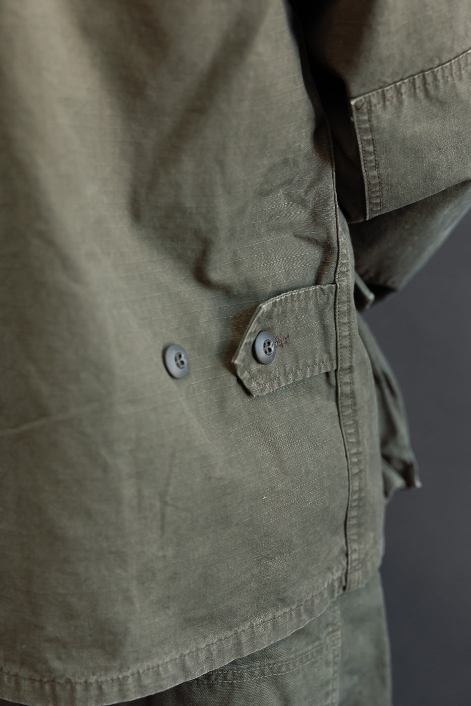Close-up of the front side of an olive green jacket showing button details and fabric texture.