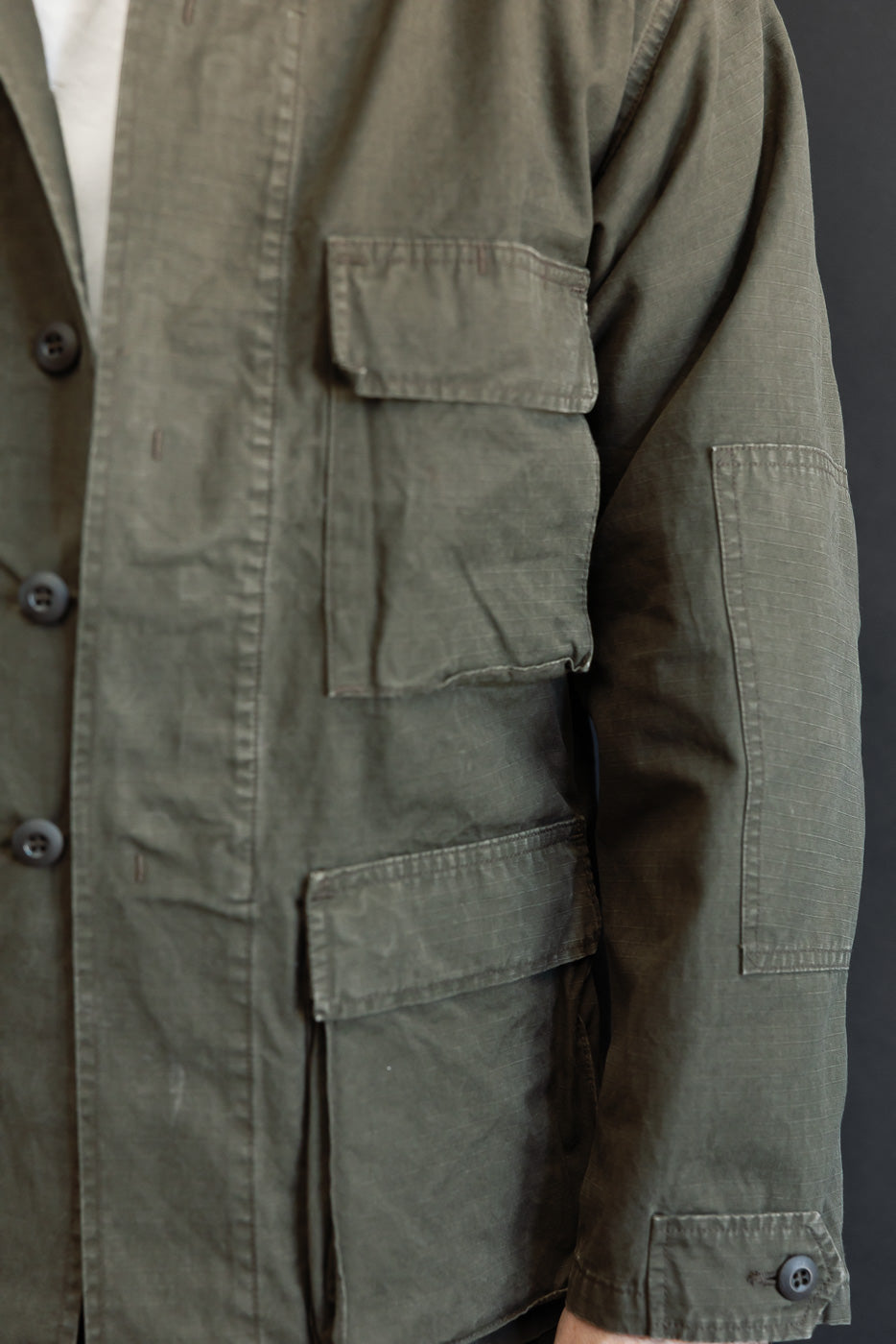 Close-up of the front left side of an olive green utility jacket showing large cargo pockets.