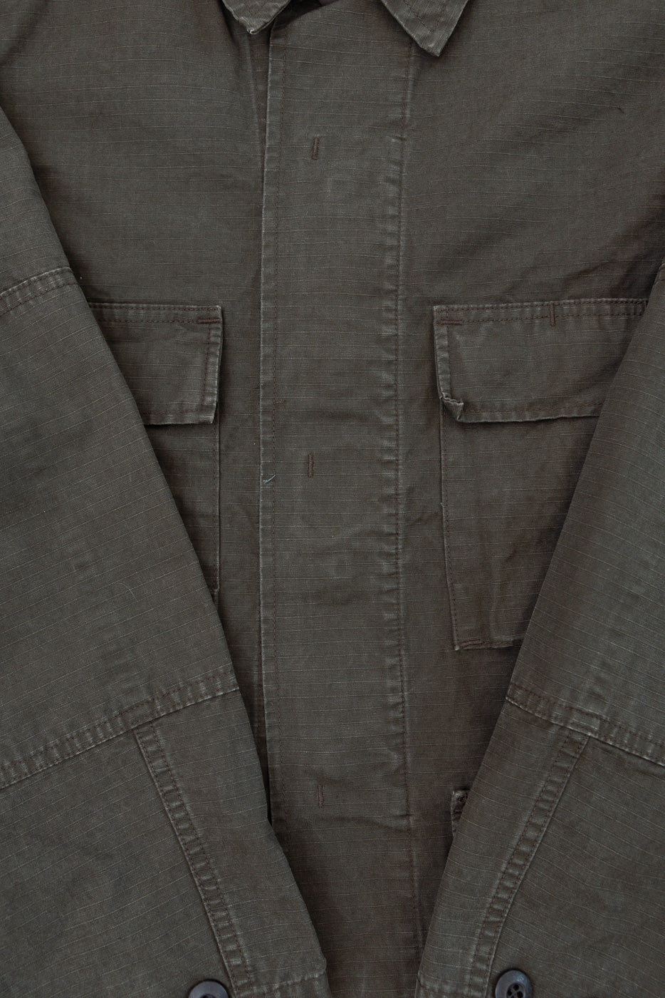 Close-up front view of a dark olive green cotton utility shirt showing fabric texture and pockets.
