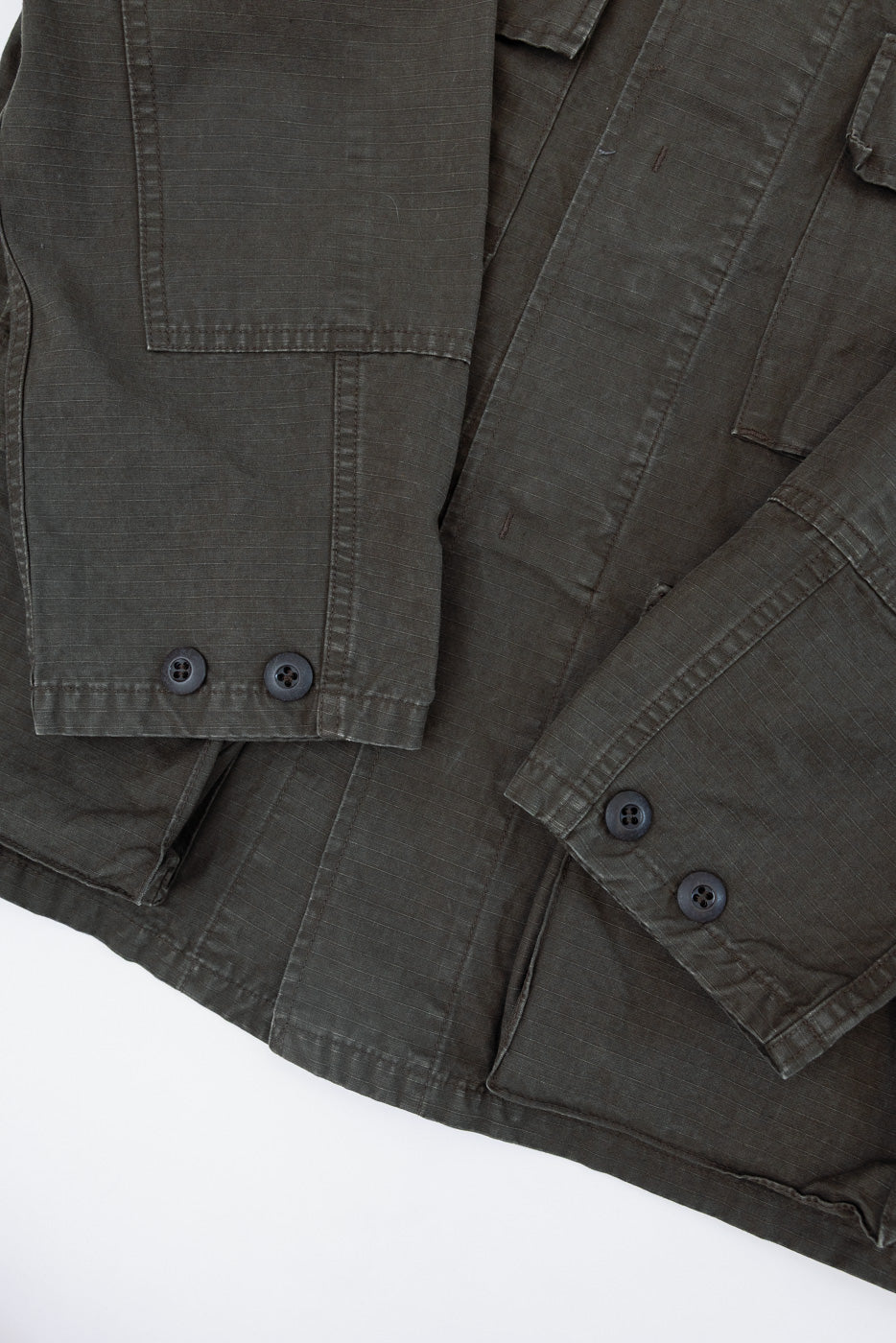 Close-up of the front of a dark olive green jacket showing sleeve buttons and fabric texture.