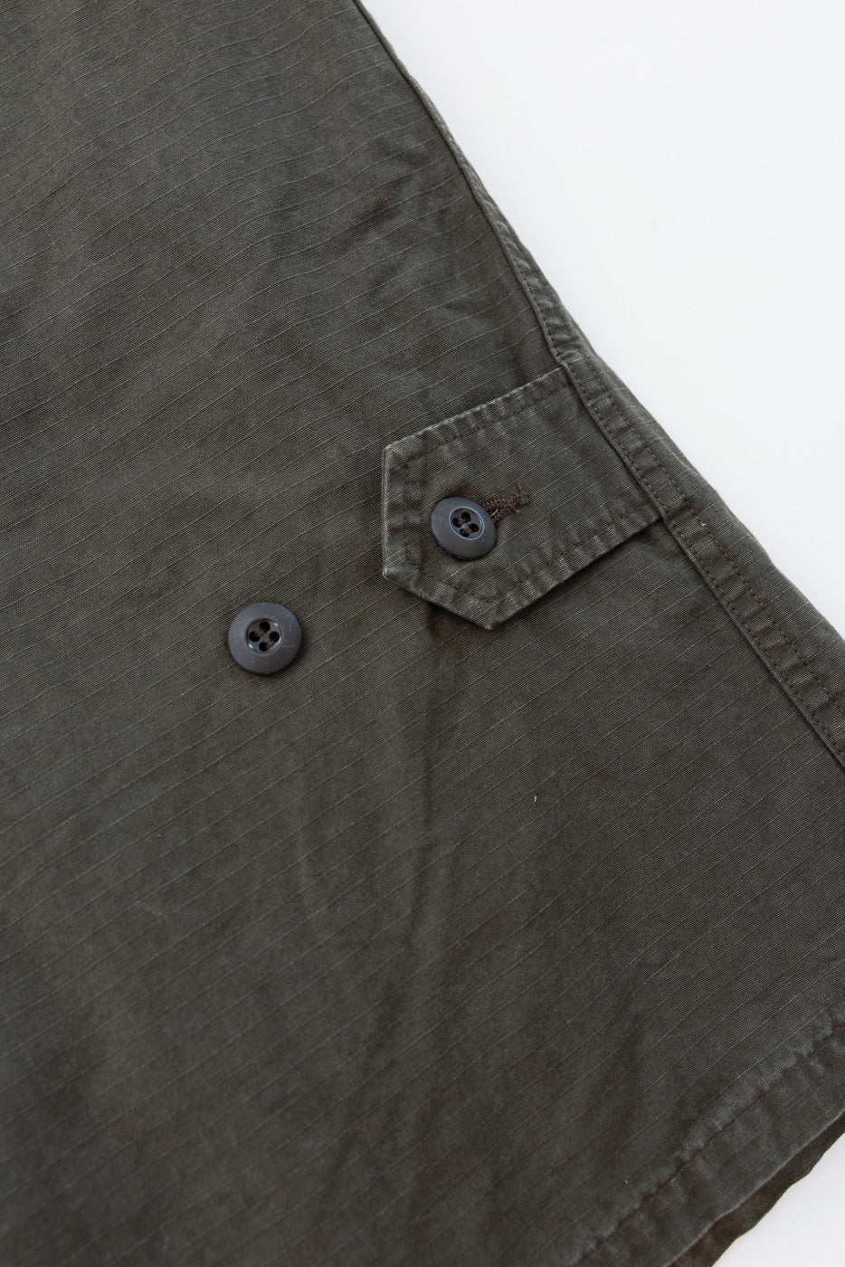 Close-up of the front of an olive green garment showing a button and pocket flap.