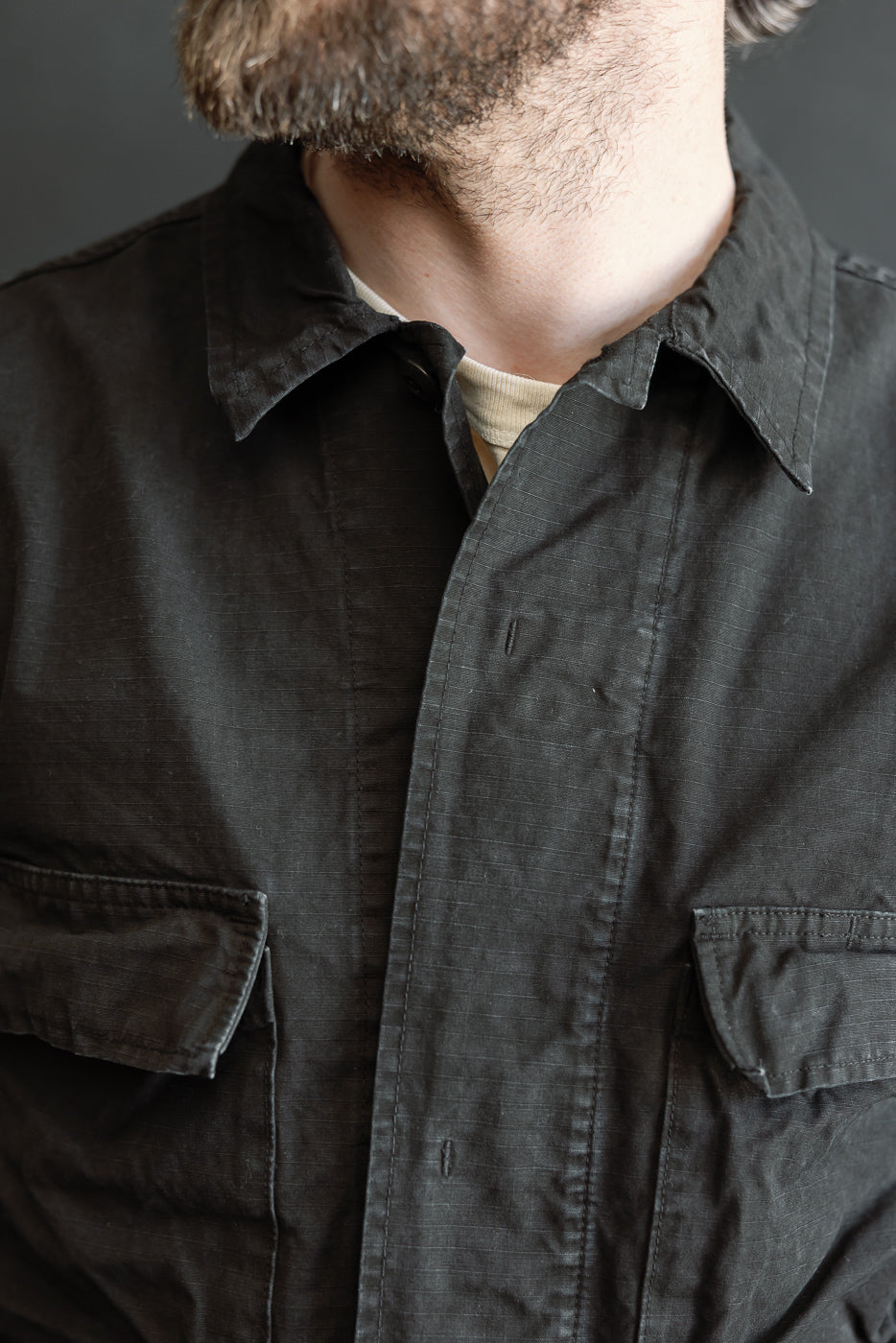 Close-up of a person wearing the 01-6110-61S - Ripstop BDU Jacket - Black Stone, showcasing the open collar and chest pockets of this Japanese ripstop fabric jacket.