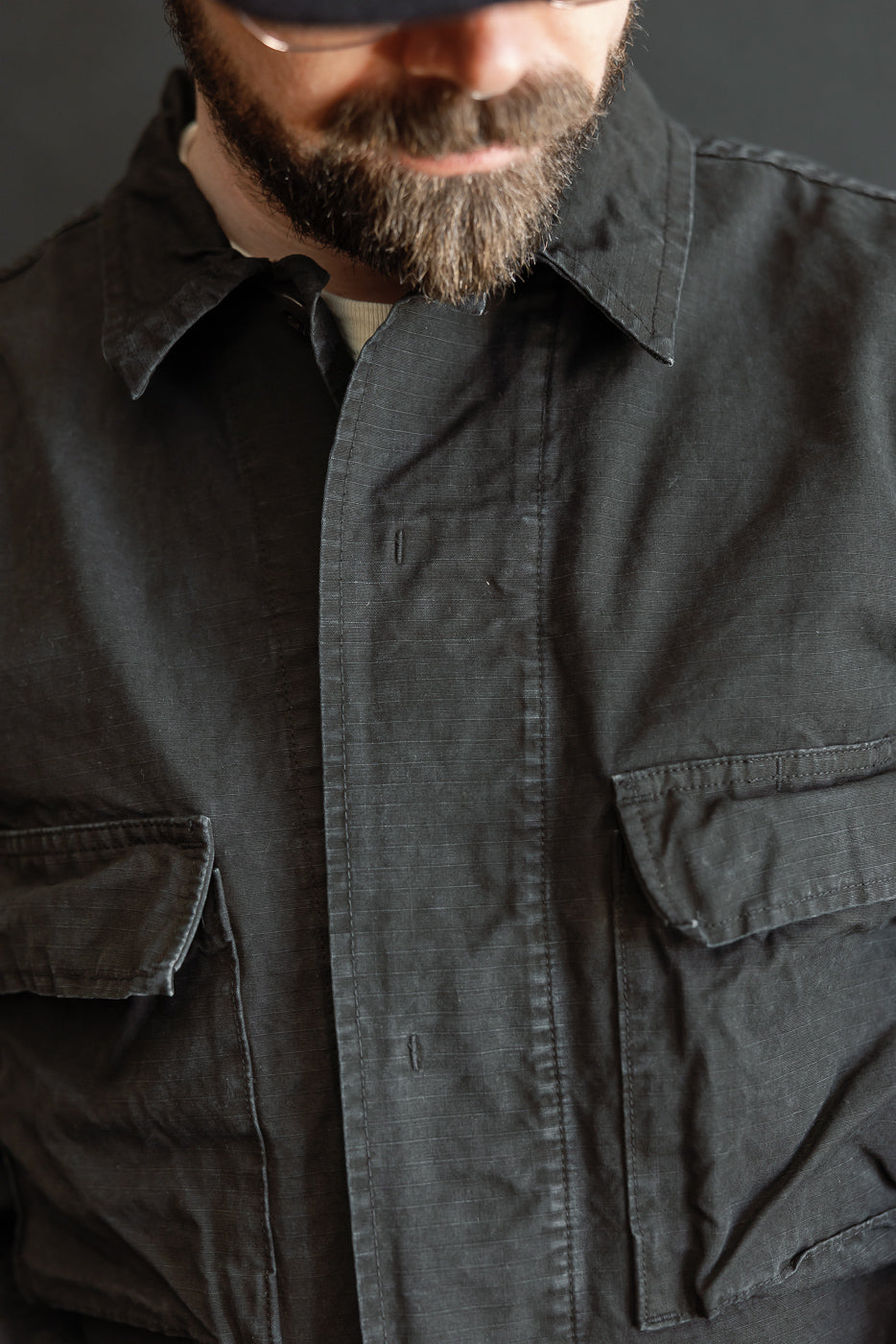 Close-up of a man wearing the 01-6110-61S - Ripstop BDU Jacket - Black Stone, showcasing its utility-style design with chest flap pockets and a rugged, black stonewashed finish.
