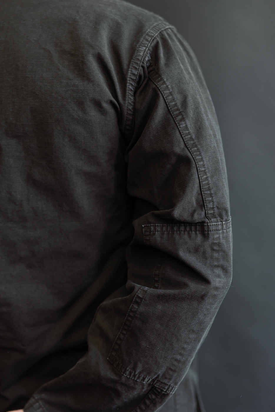 Close-up of the 01-6110-61S Ripstop BDU Jacket's textured fabric and stitching, showcasing the small patch pocket on the upper arm, highlighting orSlow's Japanese ripstop craftsmanship in black stonewashed finish.
