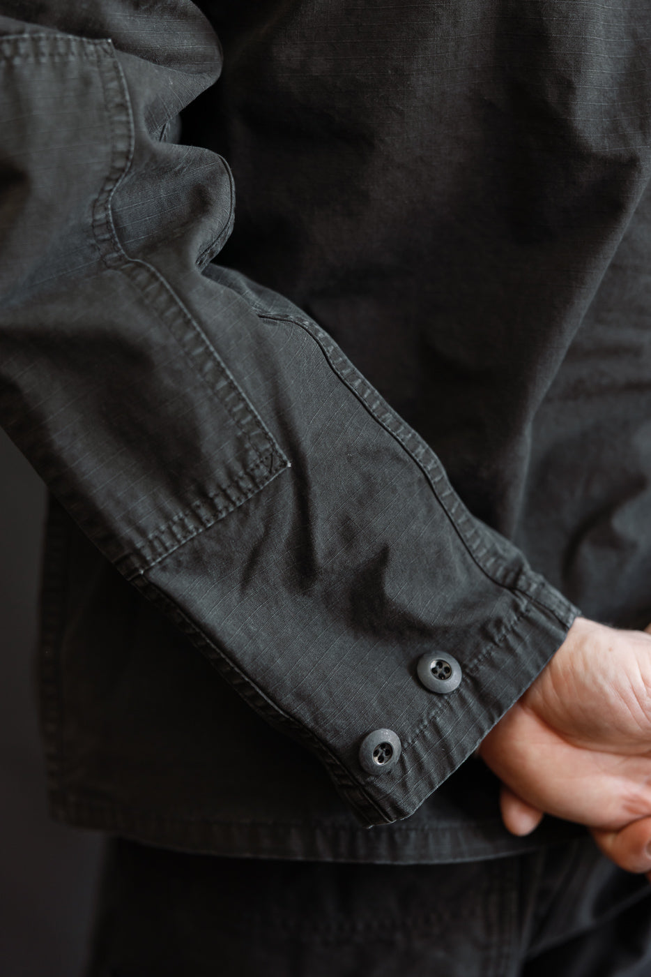 Close-up of the 01-6110-61S - Ripstop BDU Jacket - Black Stone sleeve, showcasing the dark ripstop fabric, adjustable cuff with two buttons, and pocket detail against a dark background.