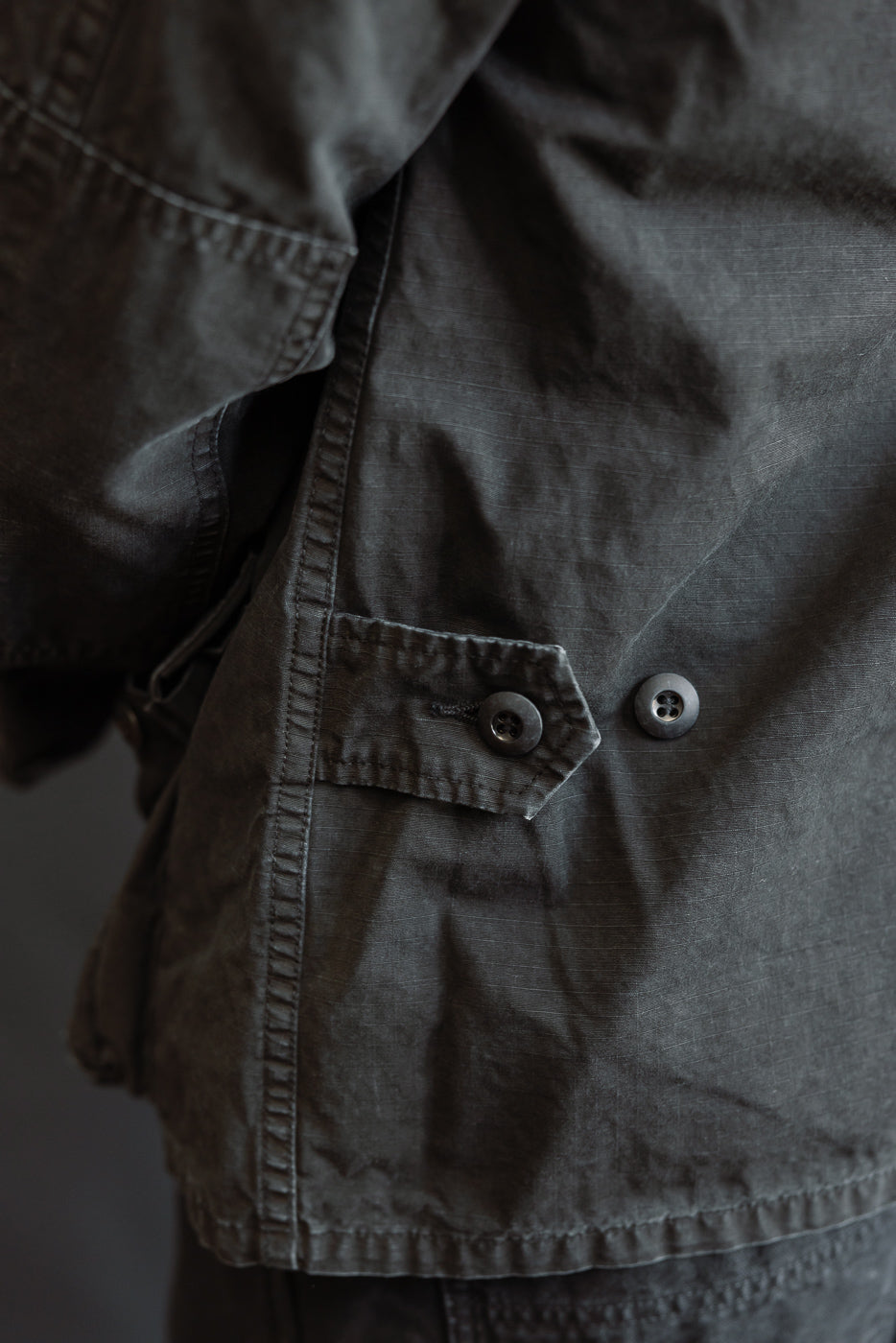 Close-up of the 01-6110-61S - Ripstop BDU Jacket - Black Stone, showcasing its dark olive-green Japanese ripstop fabric, detailed stitching, adjustable side-cinch strap, pocket flap, and hem.