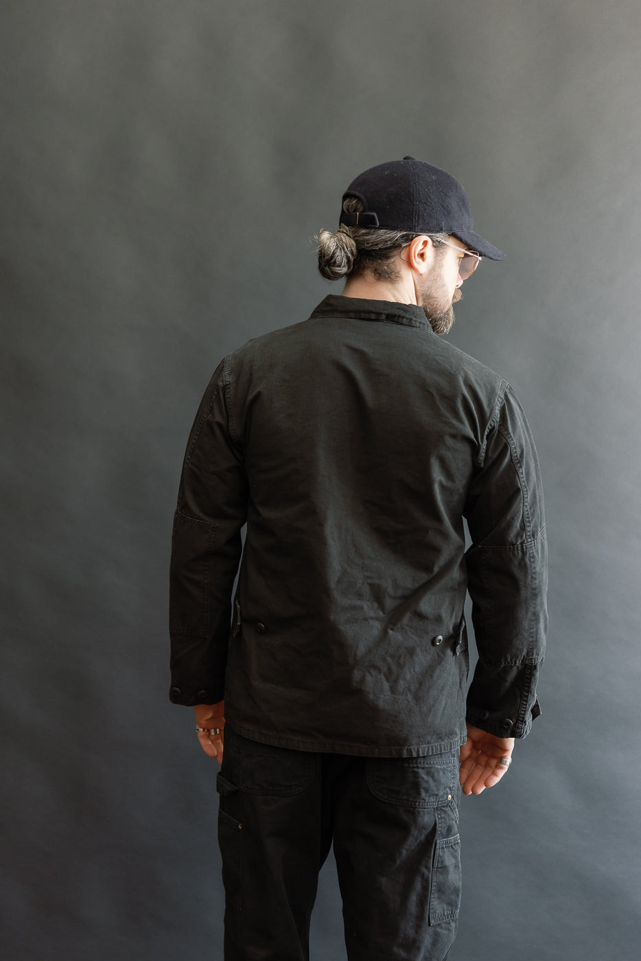 A man models the 01-6110-61S Ripstop BDU Jacket - Black Stone, showcasing its utilitarian design with patch pockets and a stonewashed finish.