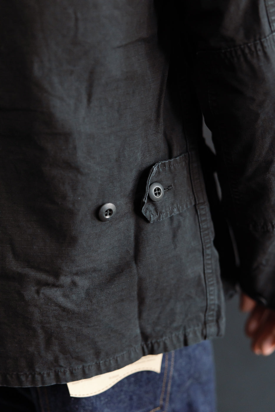 Close-up of orSlow black ripstop BDU jacket side hem and button detail, male model wearing