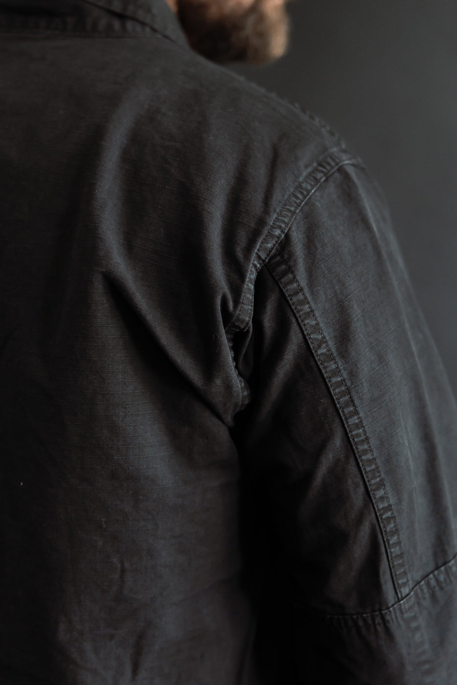 Close-up of male model's upper back and shoulder in Orslow black ripstop BDU jacket, showing fabric texture and stitching detail.