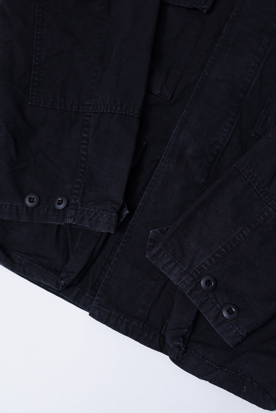 Close-up of orSlow ripstop BDU jacket black, showing front hem, sleeve cuffs, and buttons.