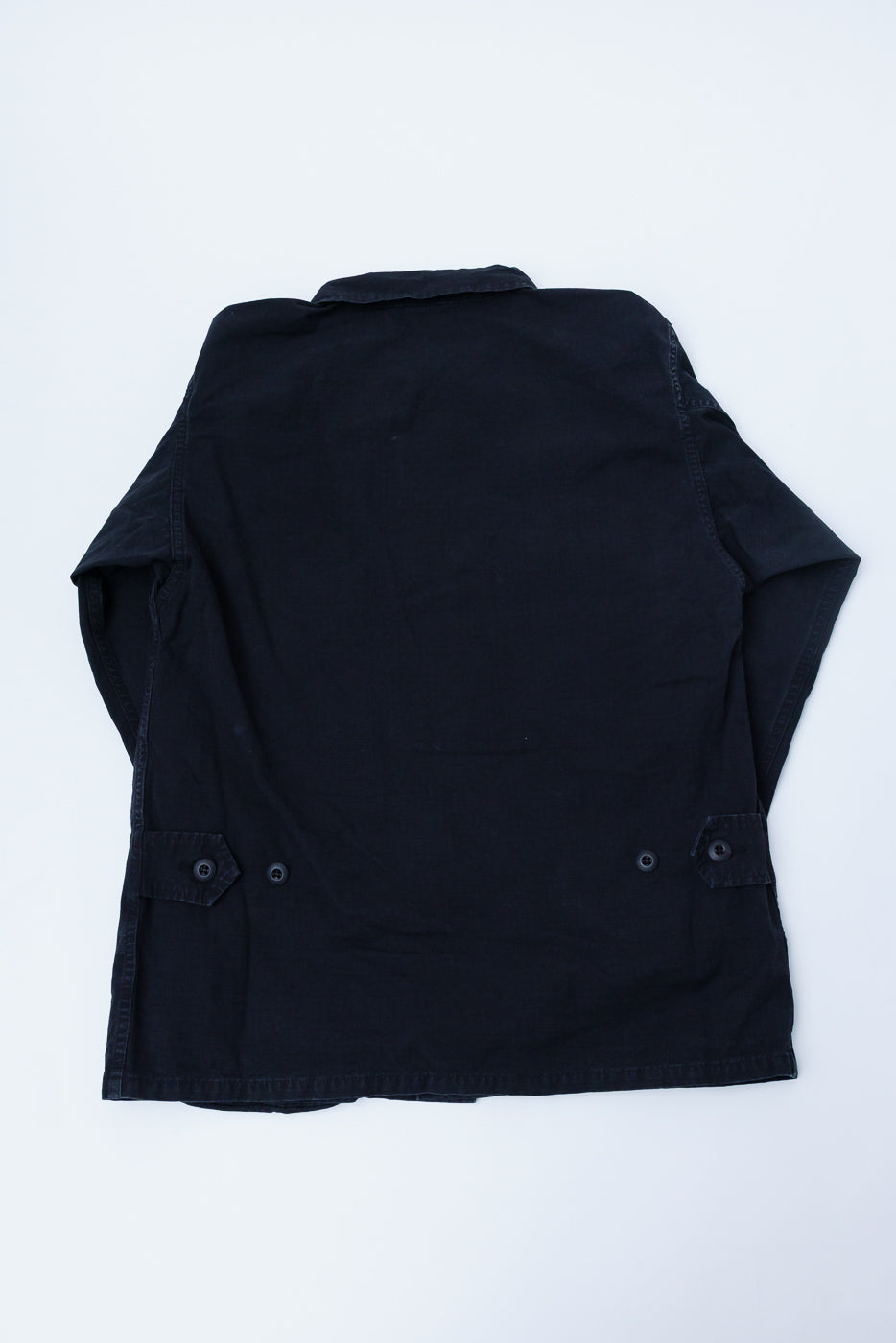 Flat lay of orSlow black ripstop BDU jacket, back side view, showing adjustable waist tabs and collar detail.